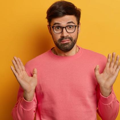 Do not involve me. Puzzled bearded man raises palms as dont want to got into trouble, bother with someone else, looks hesitant and confused, wears optical glasses and pink jumper, poses indoor